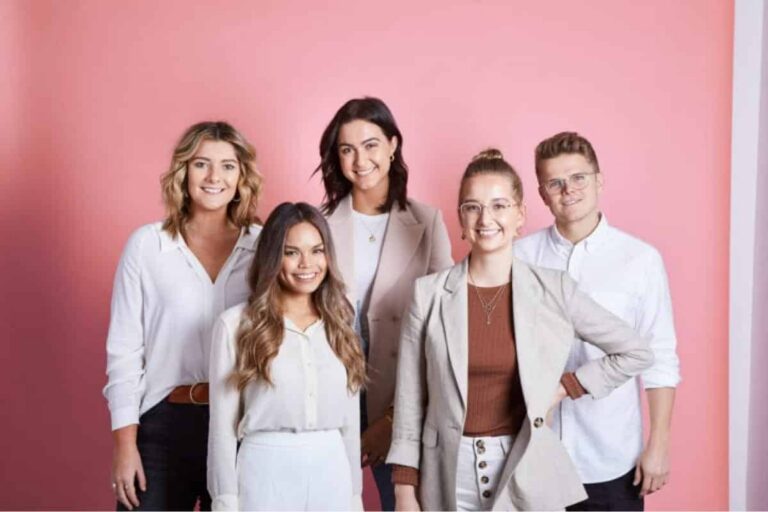 Five smiling young adults, four women and one man, in casual business attire stand in front of a pink background, representing a team specializing in financial planning. | Future Advisory